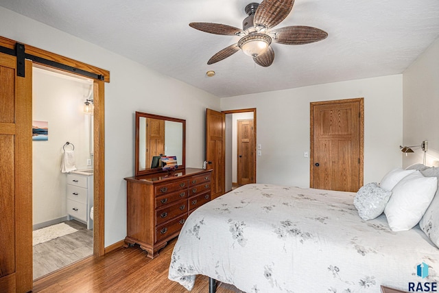 711 Britz Dr, Luverne, MN 56156 - bedroom with light wood-style flooring, a barn door, ensuite bath, baseboards, and a ceiling fan