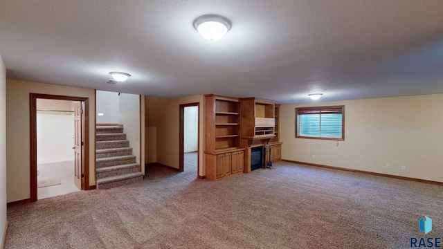 851 Regency Ct, Brookings, SD 57006 - unfurnished living room with a glass covered fireplace, light colored carpet, stairs, and baseboards