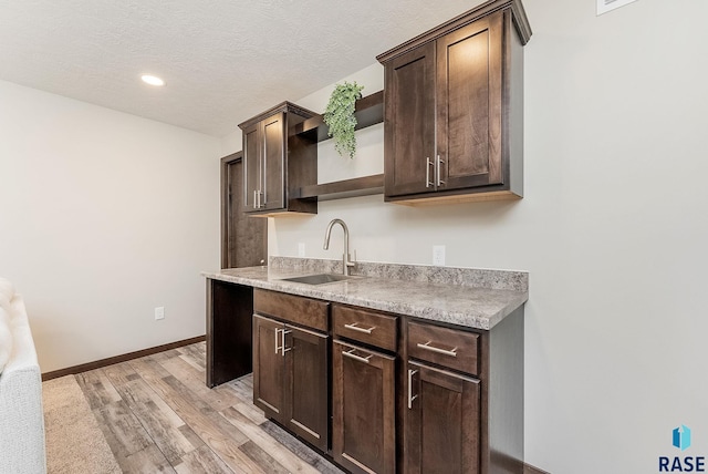 kitchen featuring a sink, open shelves, dark brown cabinets, baseboards, and a textured ceiling