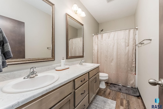 bathroom featuring wood finished floors, double vanity, toilet, and curtained shower