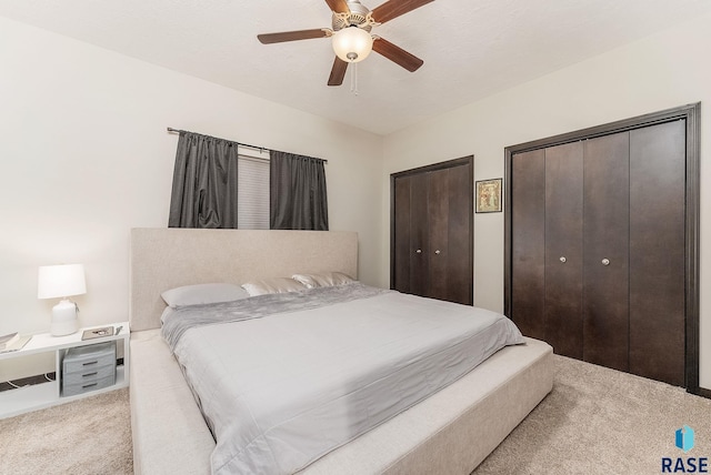 bedroom with light colored carpet, multiple closets, and ceiling fan
