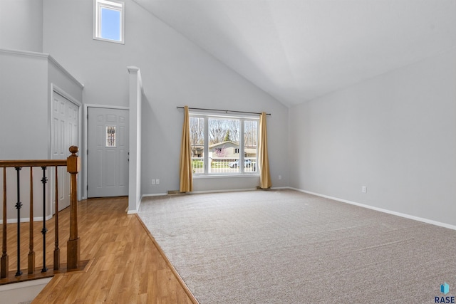 unfurnished living room with high vaulted ceiling, baseboards, and light wood-style floors