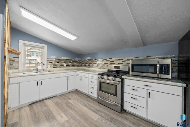 kitchen with stainless steel appliances, a sink, lofted ceiling, tasteful backsplash, and light wood-type flooring