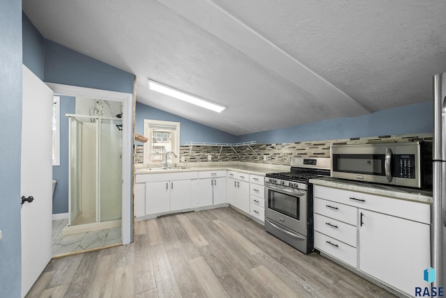 kitchen featuring stainless steel appliances, a sink, lofted ceiling, light wood-style flooring, and tasteful backsplash