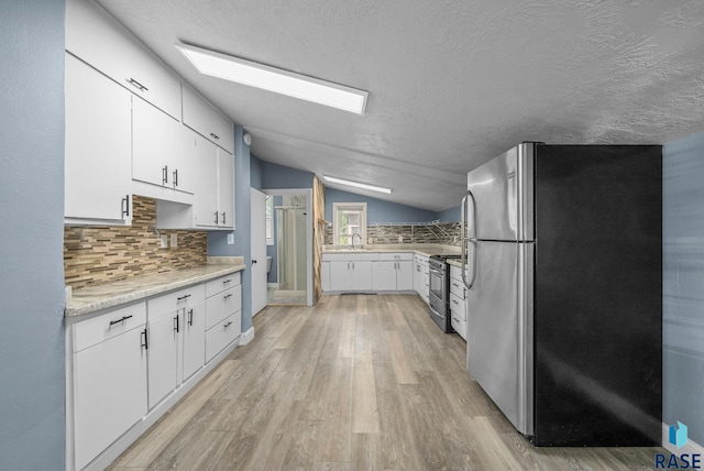 kitchen with stainless steel appliances, vaulted ceiling, backsplash, light wood-style flooring, and white cabinetry