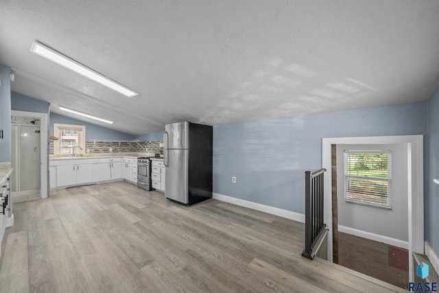 kitchen with appliances with stainless steel finishes, light countertops, a sink, vaulted ceiling, and light wood-type flooring
