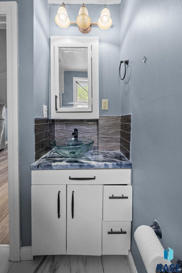 bathroom featuring decorative backsplash, vanity, marble finish flooring, and baseboards