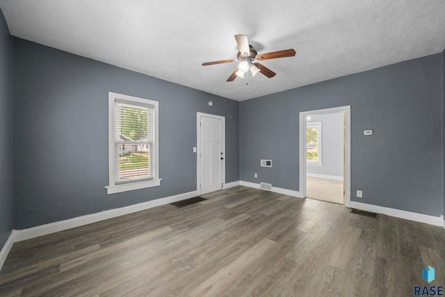 empty room featuring plenty of natural light, ceiling fan, wood finished floors, baseboards, and a textured ceiling