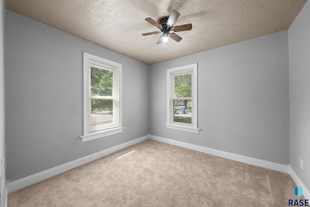 empty room with light carpet, a ceiling fan, a textured ceiling, and baseboards