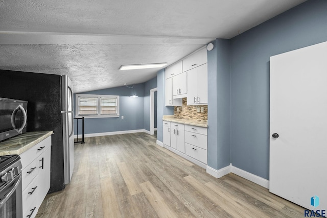 kitchen with stainless steel appliances, lofted ceiling, light wood-style flooring, white cabinetry, and baseboards