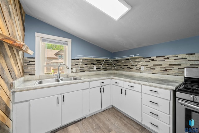 kitchen featuring stainless steel range with electric stovetop, a sink, lofted ceiling, backsplash, and light countertops