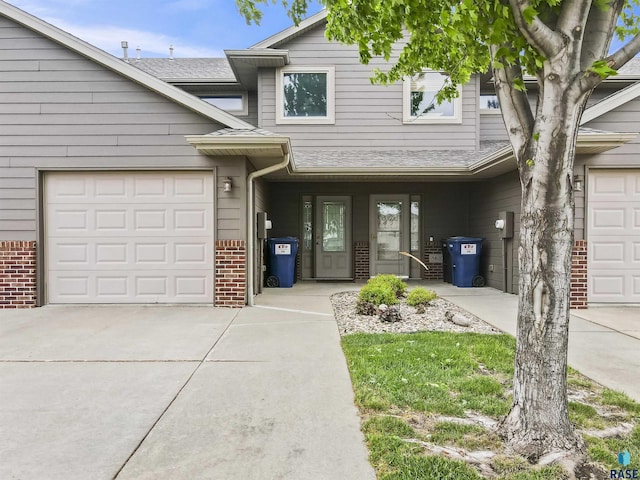view of front facade featuring concrete driveway, brick siding, a shingled roof, and a garage