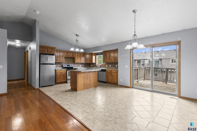 kitchen with appliances with stainless steel finishes, a chandelier, a kitchen island, tasteful backsplash, and lofted ceiling