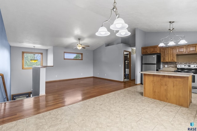 kitchen featuring appliances with stainless steel finishes, a chandelier, a kitchen island, decorative backsplash, and vaulted ceiling