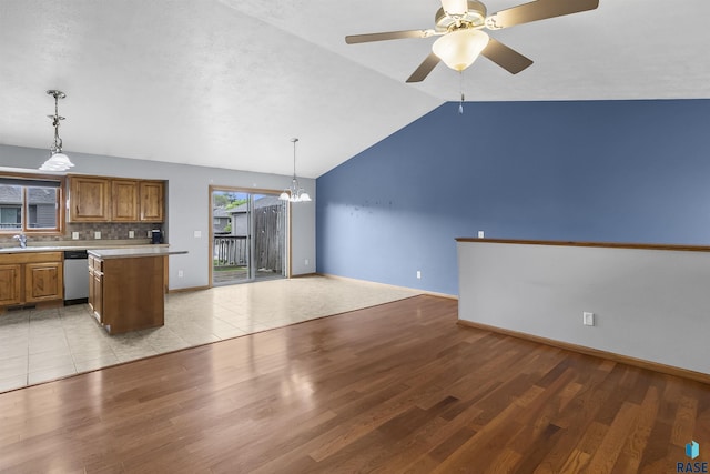 kitchen with stainless steel dishwasher, brown cabinets, a sink, light countertops, and lofted ceiling