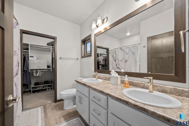 full bath featuring wood finished floors, toilet, double vanity, and a walk in closet