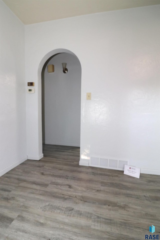 empty room featuring arched walkways and wood finished floors