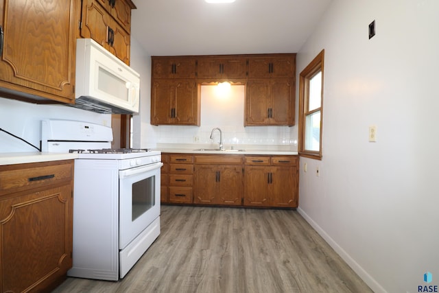 kitchen featuring white appliances, a sink, light wood-style floors, brown cabinets, and light countertops