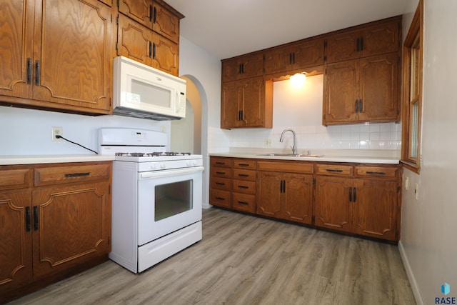 kitchen with white appliances, a sink, light wood-type flooring, and light countertops