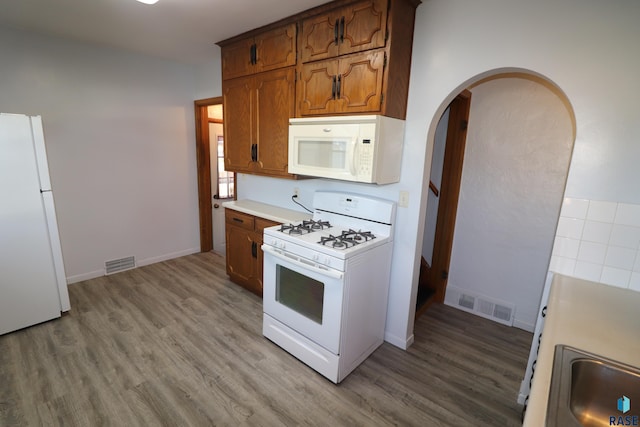 kitchen with white appliances, light wood finished floors, light countertops, and arched walkways