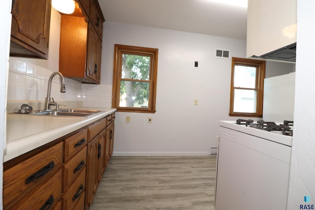kitchen featuring a sink, white gas range oven, light wood-style floors, backsplash, and brown cabinetry