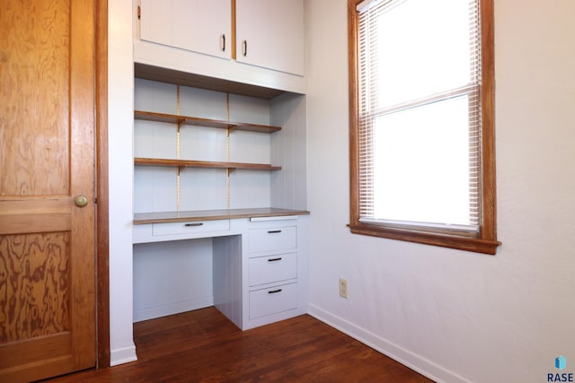 unfurnished office featuring built in desk, dark wood finished floors, plenty of natural light, and baseboards