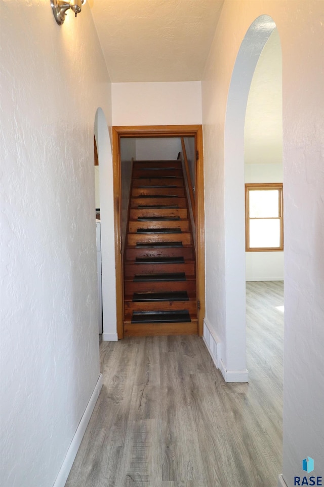 stairs featuring arched walkways, wood finished floors, and baseboards