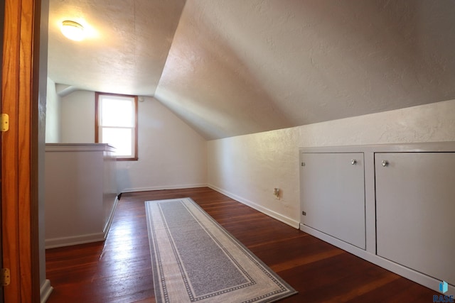 bonus room with a textured ceiling, vaulted ceiling, dark wood-style floors, baseboards, and a textured wall