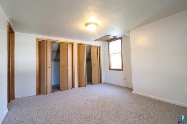 unfurnished bedroom featuring carpet, multiple closets, and baseboards