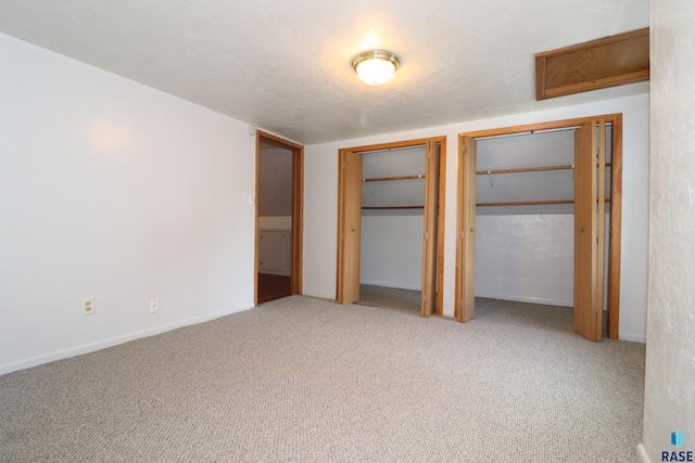 unfurnished bedroom with two closets, carpet floors, and baseboards