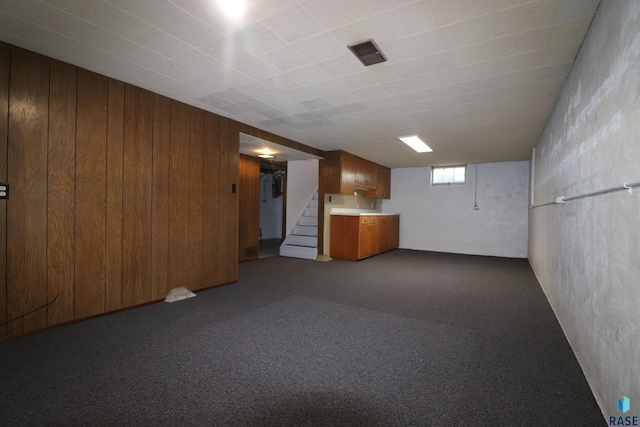 below grade area featuring wood walls, stairs, and dark carpet
