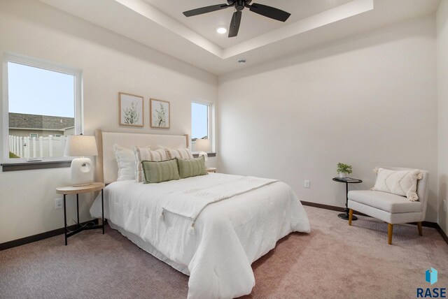 bedroom featuring light colored carpet, baseboards, a tray ceiling, recessed lighting, and ceiling fan