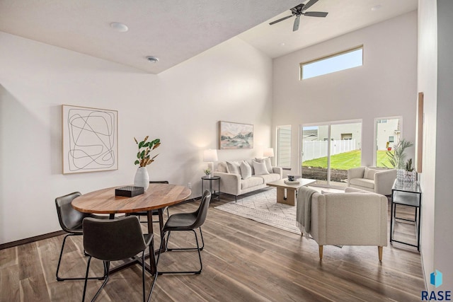 dining space with wood finished floors, a ceiling fan, baseboards, and a towering ceiling