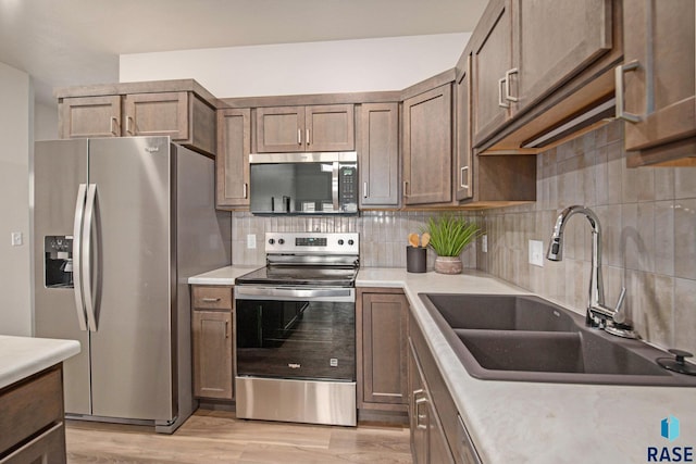 kitchen featuring appliances with stainless steel finishes, a sink, decorative backsplash, light wood finished floors, and light countertops
