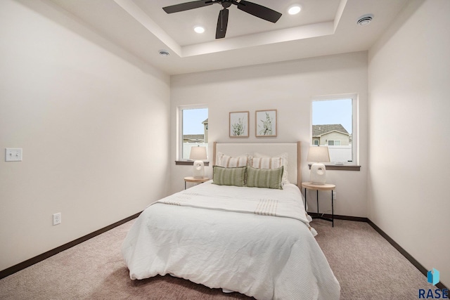 carpeted bedroom featuring multiple windows, baseboards, ceiling fan, a raised ceiling, and recessed lighting