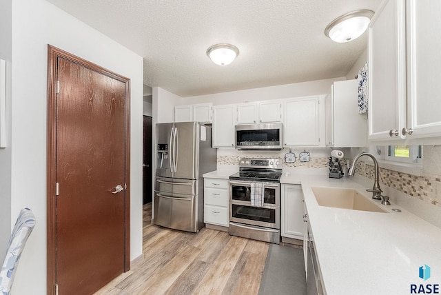 kitchen featuring stainless steel appliances, a sink, backsplash, light wood-type flooring, and light countertops