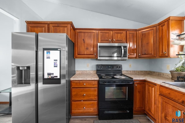 kitchen featuring stainless steel appliances, lofted ceiling, light countertops, brown cabinets, and wood finished floors