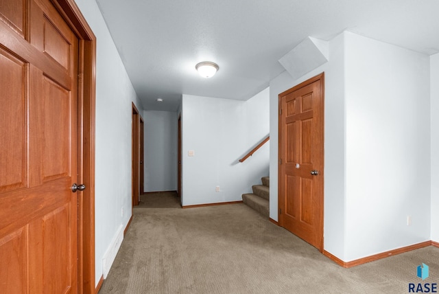 hall featuring light colored carpet, baseboards, and stairway