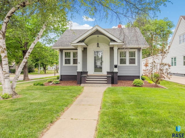 bungalow-style house featuring a front yard, a shingled roof, and a chimney