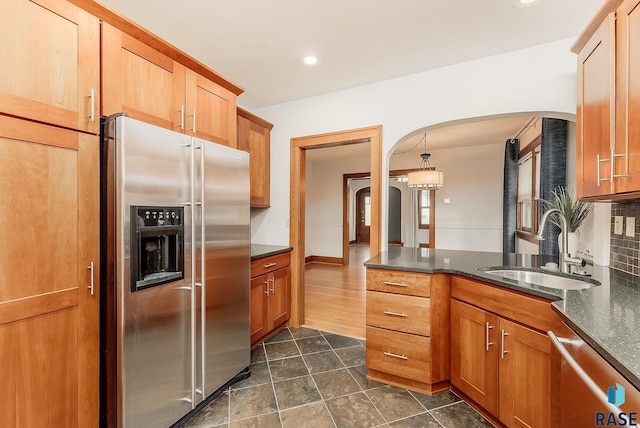 kitchen featuring stainless steel appliances, a sink, arched walkways, backsplash, and dark stone countertops