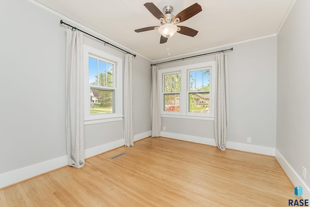 spare room featuring ornamental molding, light wood-type flooring, plenty of natural light, ceiling fan, and baseboards