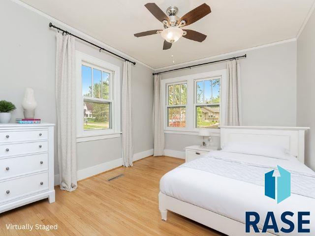 bedroom featuring ornamental molding, baseboards, multiple windows, light wood-type flooring, and a ceiling fan