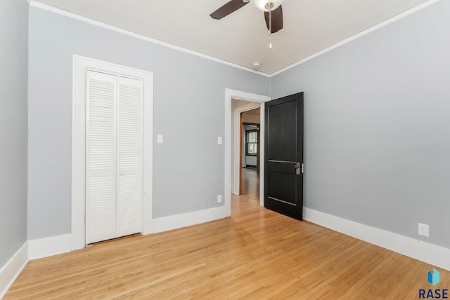 unfurnished bedroom featuring crown molding, light wood-style floors, baseboards, and a closet