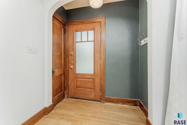 entryway featuring arched walkways, light wood finished floors, and baseboards