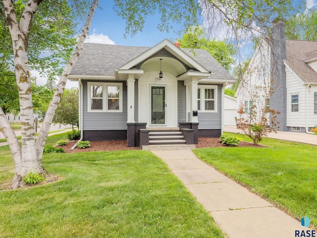 bungalow-style house featuring a front lawn, roof with shingles, and a garage