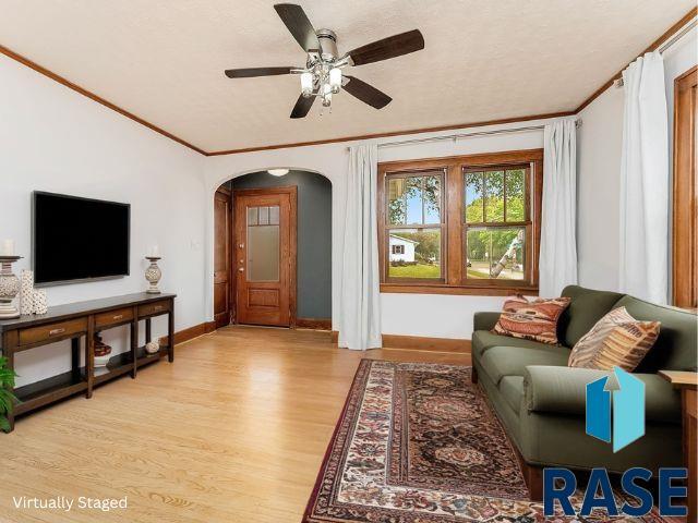 living area featuring light wood-style floors, arched walkways, baseboards, ceiling fan, and ornamental molding
