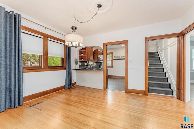 unfurnished living room featuring light wood-style floors, baseboards, a sink, and a chandelier