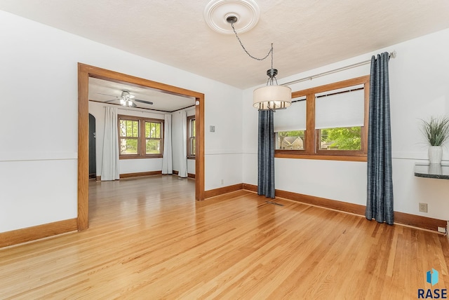 spare room featuring light wood-type flooring, baseboards, arched walkways, and a ceiling fan
