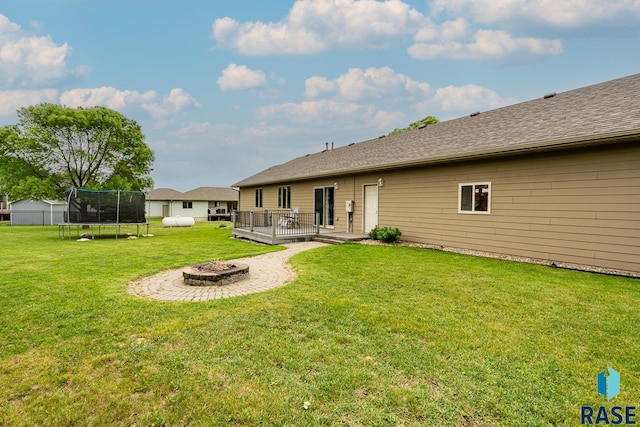 811 Southview Dr, Larchwood, IA 51241 - back of property with an outdoor fire pit, a wooden deck, a trampoline, and a lawn