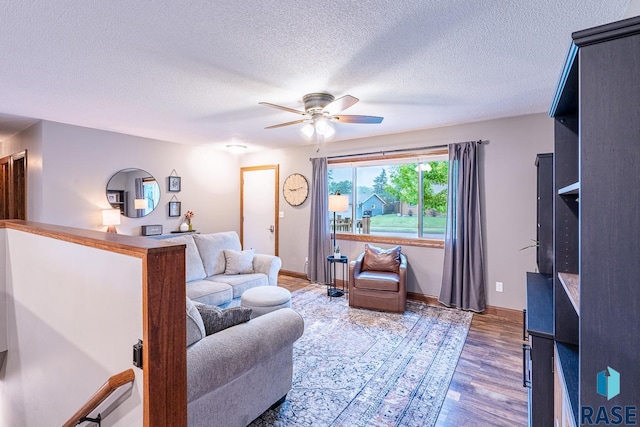 living room featuring ceiling fan, wood finished floors, baseboards, and a textured ceiling